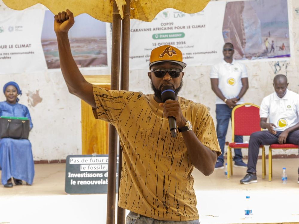 Un militant, poing levé, prend la parole lors de la caravane pour le climat à Bargny